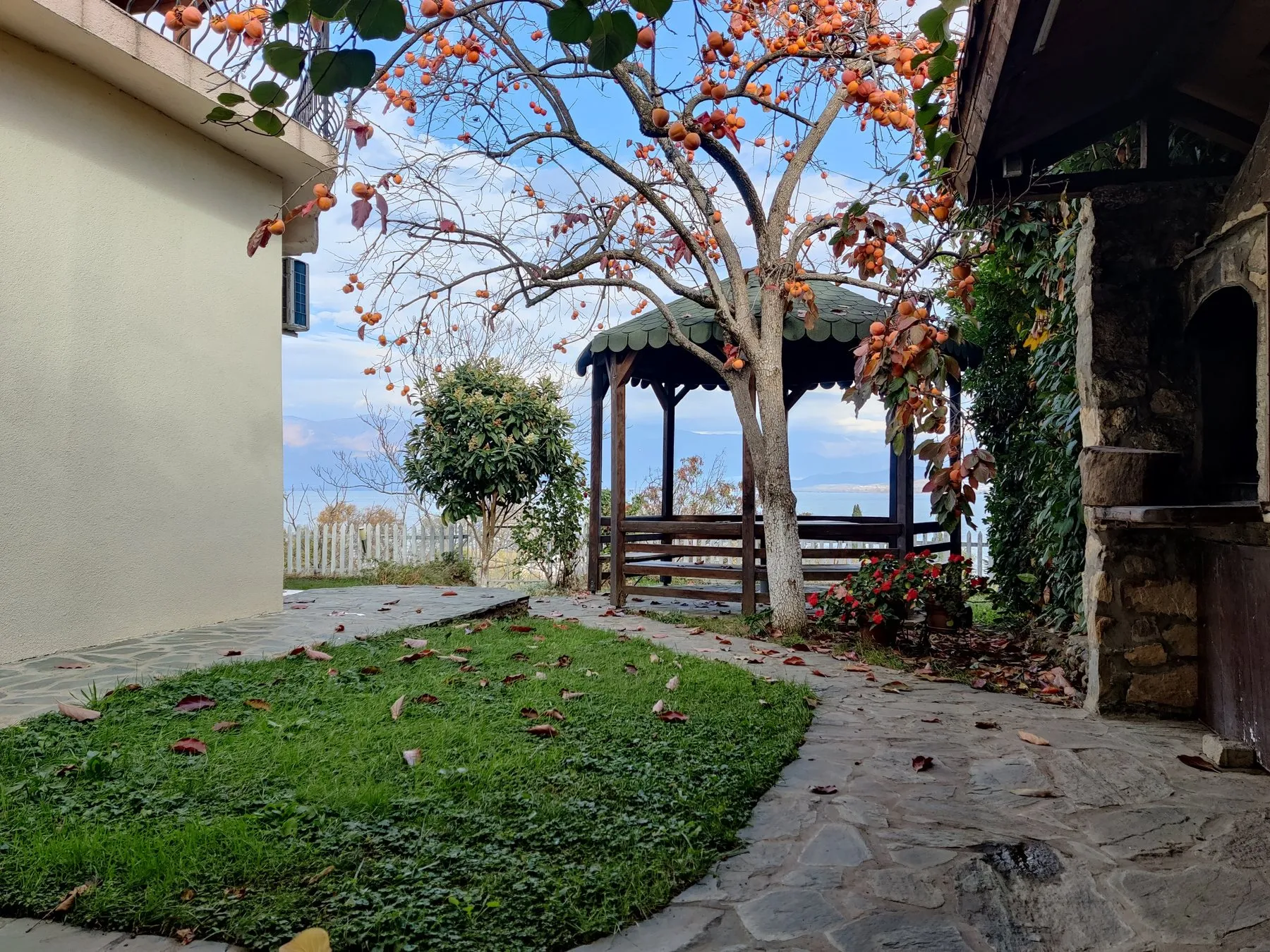 Garden courtyard with a pergola, persimmon tree, flowers, and lake view