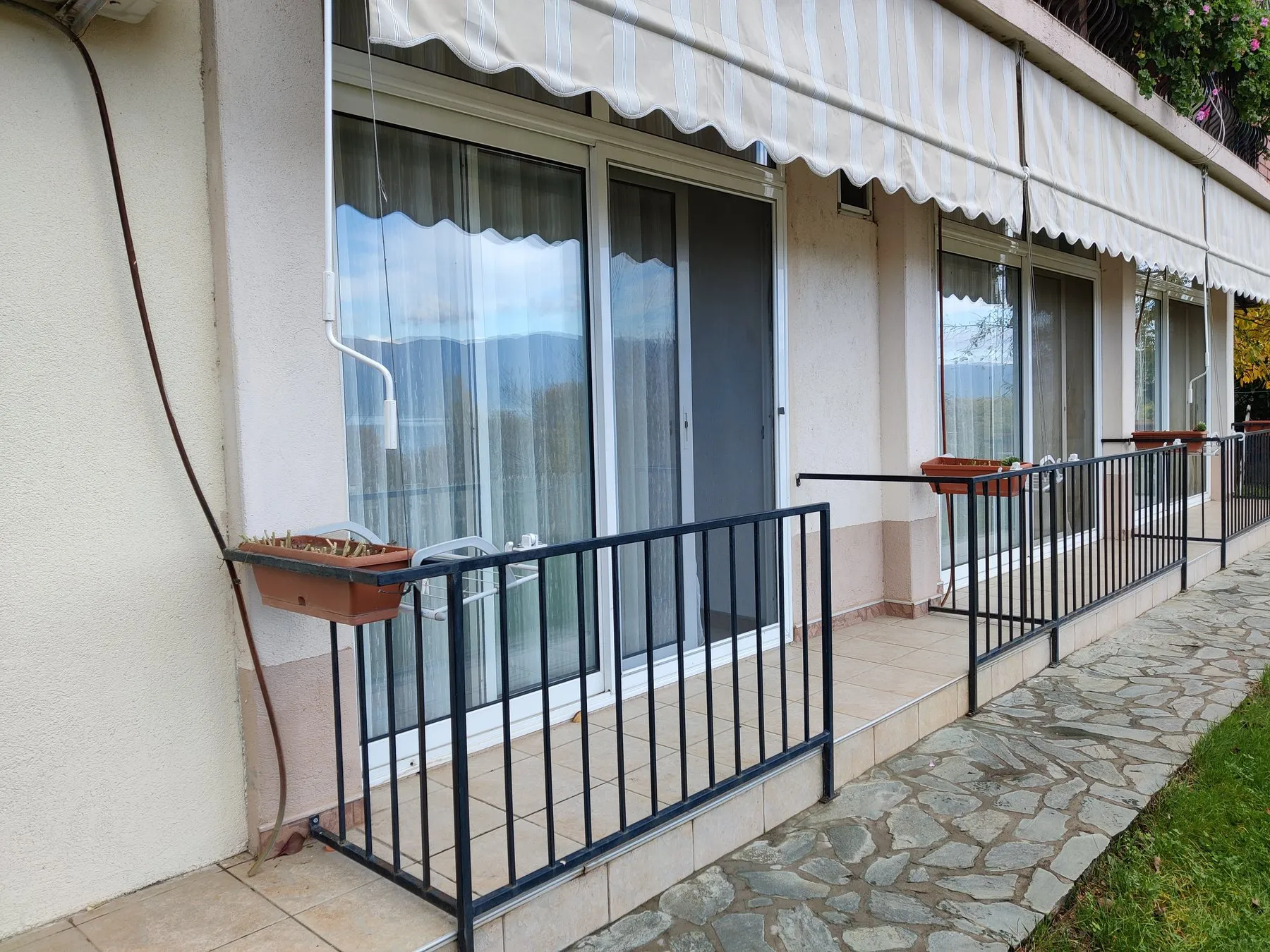 Ground-floor terrace with awnings, flower boxes, and a stone walkway